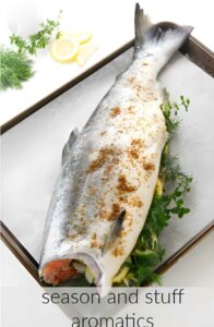 Adding seasonings and herbs to the middle of a whole salmon.