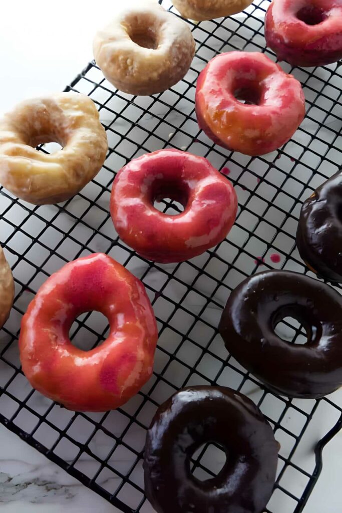 Assorted glazed donuts on a black cooling rack over white background.