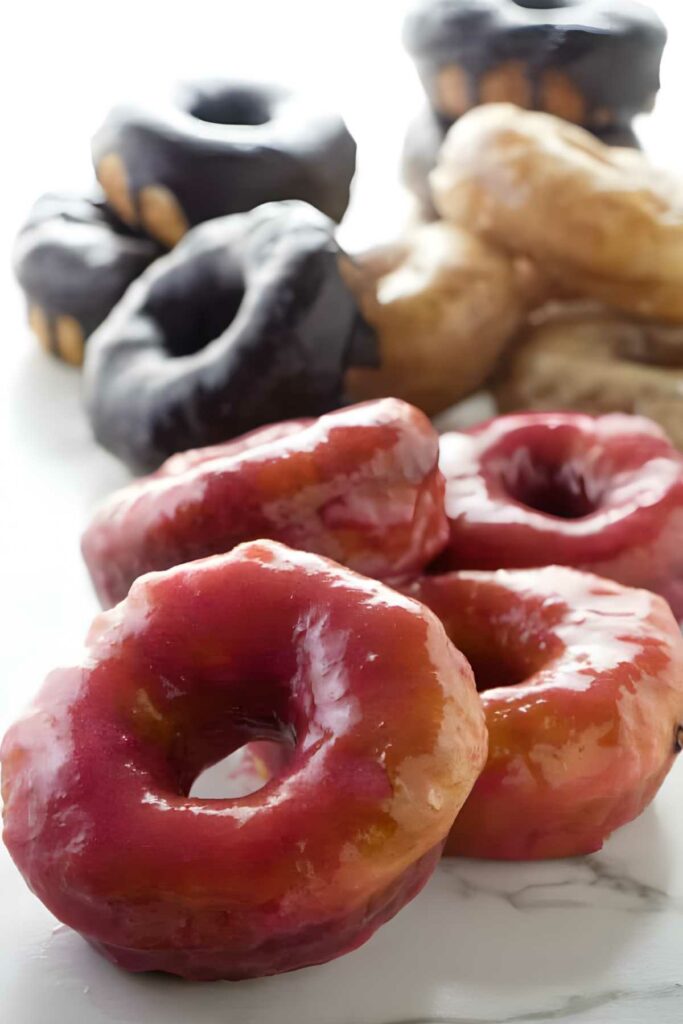 Close-up of shiny pink and brown glazed donuts stacked on white surface.