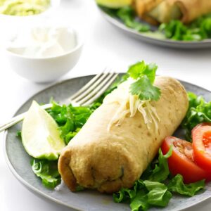 Chimichanga with cheese, cilantro, lettuce, tomato; dips in background.