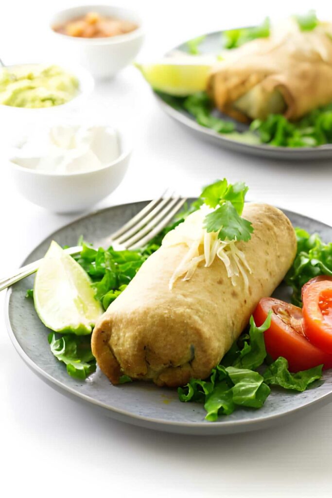 Chimichanga with cheese, cilantro, lettuce, tomato; dips in background.