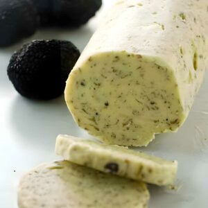 Compound butter log with herbs and truffles, sliced, black truffles behind.