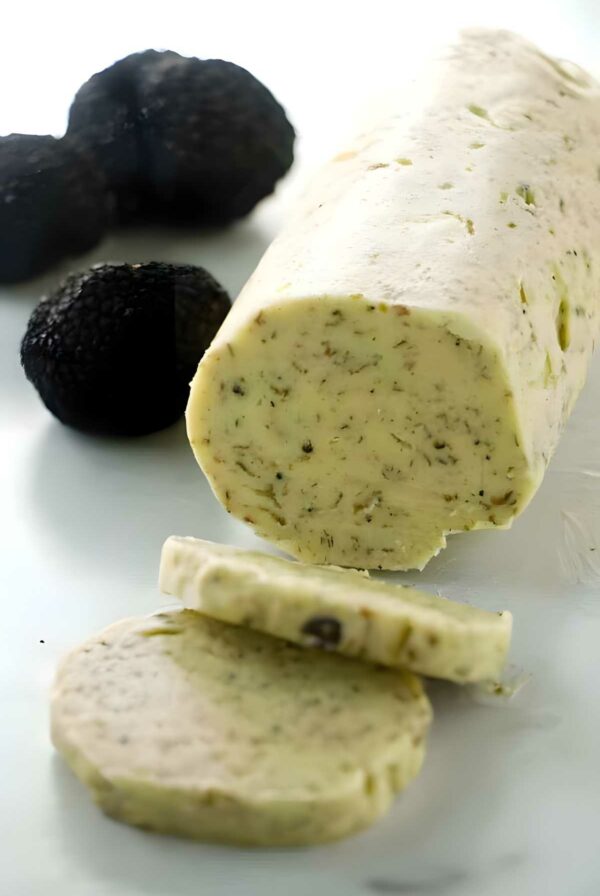 Compound butter log with herbs and truffles, sliced, black truffles behind.