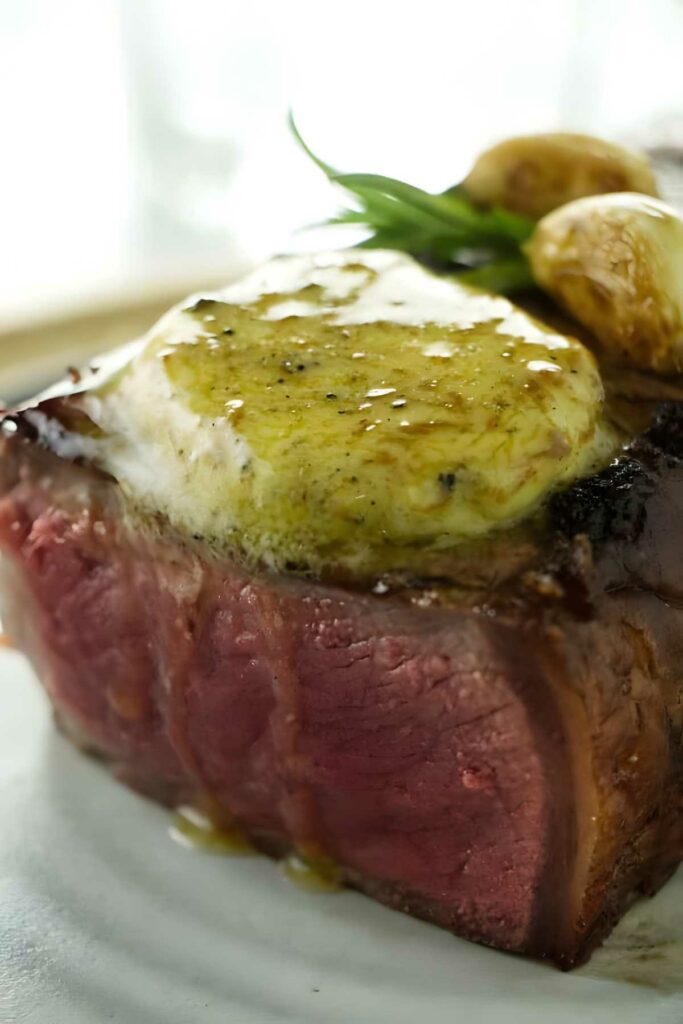 Medium-rare steak with melting truffle butter, garnished with herbs and potatoes.