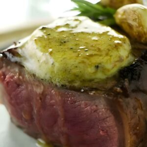 Rare steak with melting herb butter, roasted potatoes, and fresh herbs.