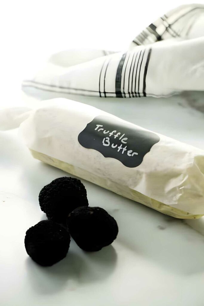 Truffle butter log beside whole black truffles and striped white cloth.