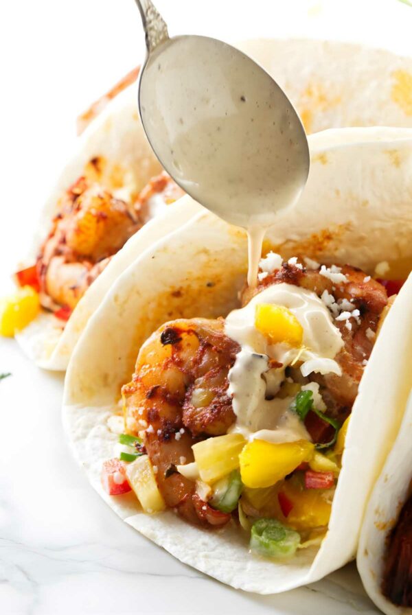 Spoon drizzling creamy sauce on spicy shrimp taco.