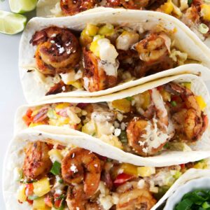 Three shrimp tacos with mango salsa, cheese, limes, and green onions.