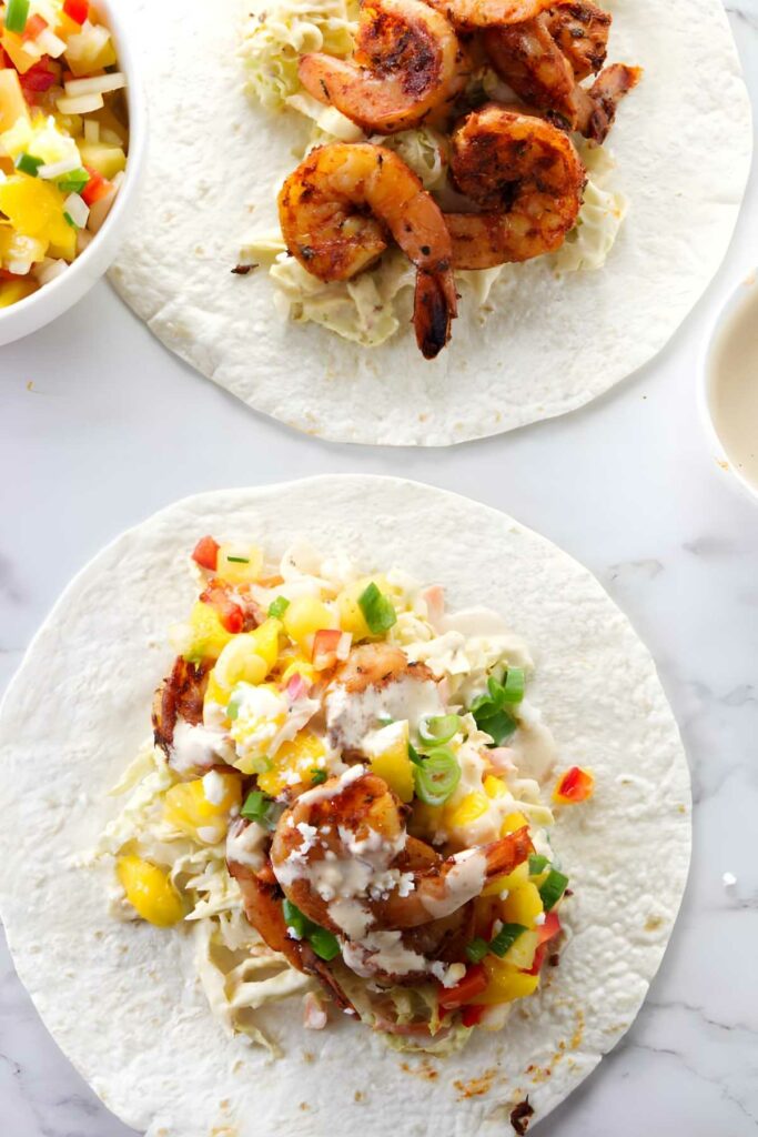 Two blackened shrimp tacos with vegetables and pineapple salsa; bowl of salsa nearby.