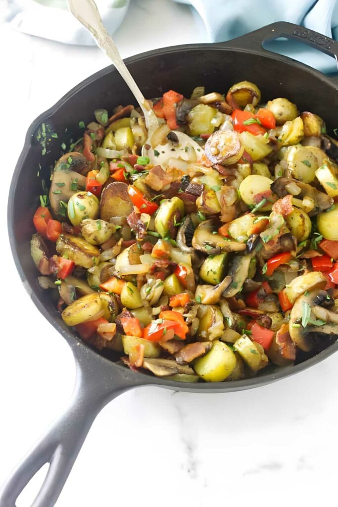 Colorful vegetable hash in cast iron skillet with potatoes, peppers, and spoon.