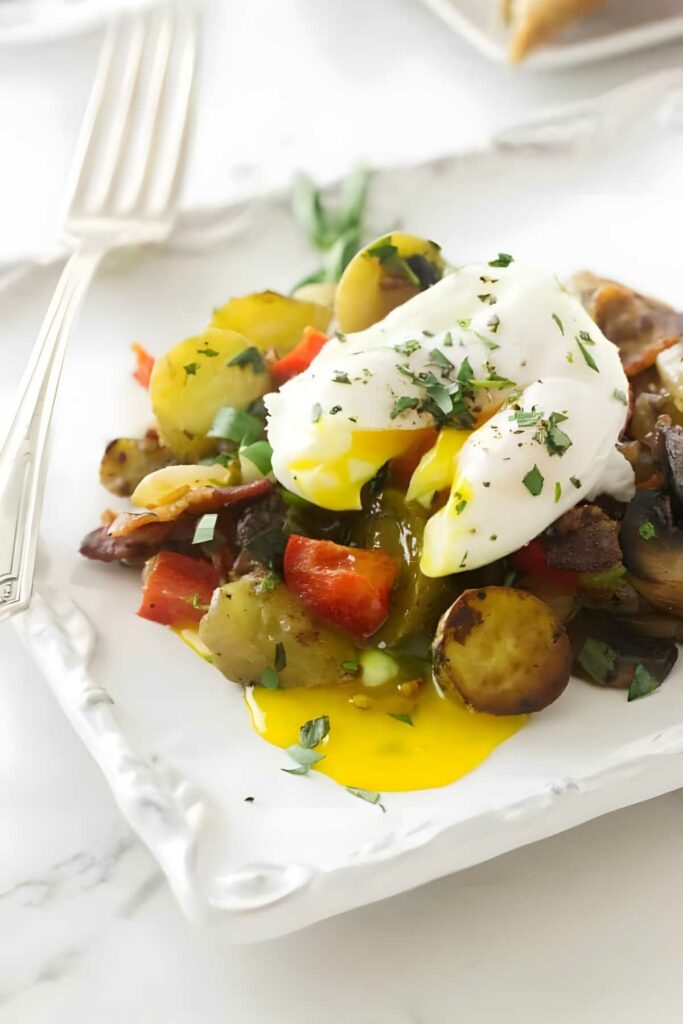 Poached egg on potato hash with vegetables and herbs, fork beside plate.