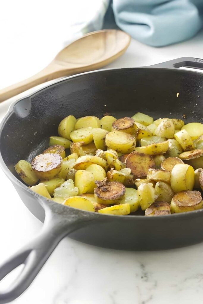 Sautéed potatoes and onions in skillet with wooden spoon and blue cloth.
