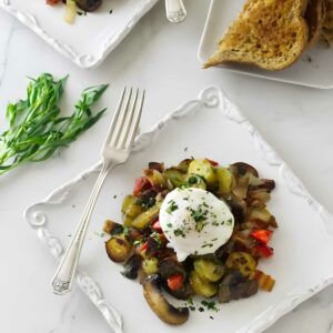 Sautéed vegetables with poached egg on plate, toast and herbs behind.