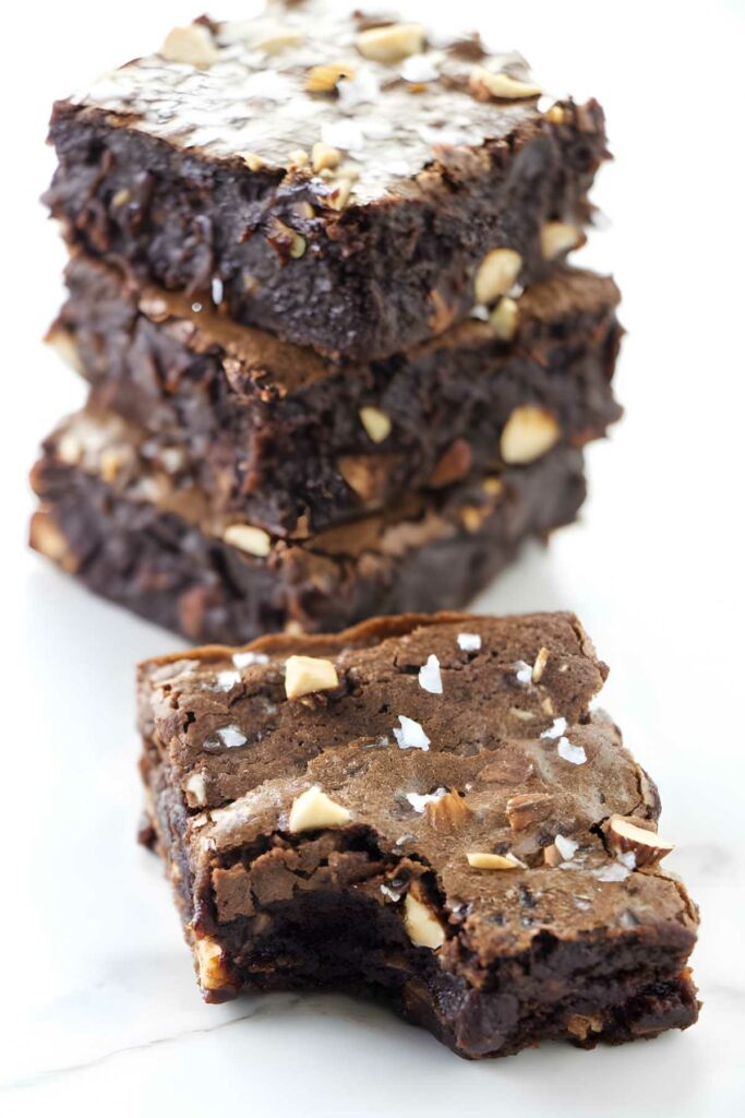 Stacked chocolate brownies with nuts and sea salt, one with bite.