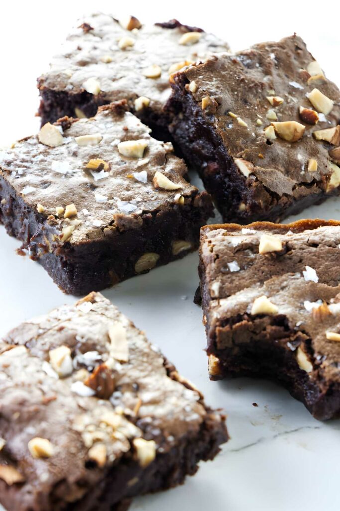 Four nut-topped chocolate brownies, one bitten, showing fudgy interior.