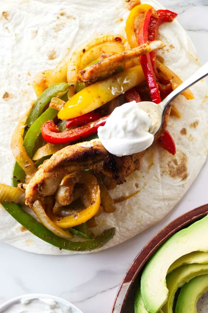 Grilled chicken fajita on tortilla with peppers, onions, sour cream, avocado.