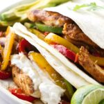 Chicken fajitas with grilled strips, colorful peppers, avocado, lime, and sour cream.