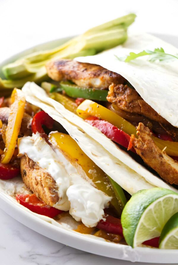 Chicken fajitas with grilled strips, colorful peppers, avocado, lime, and sour cream.