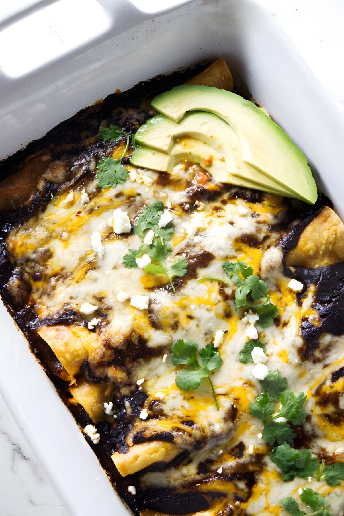 Crowd pleasing shredded chicken enchiladas with mole sauce and avocado.