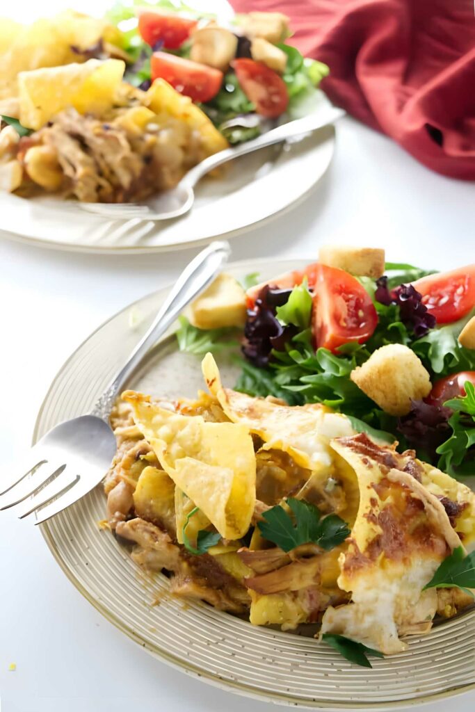 Cheesy nacho casserole with chips, parsley, and side salad on plates.
