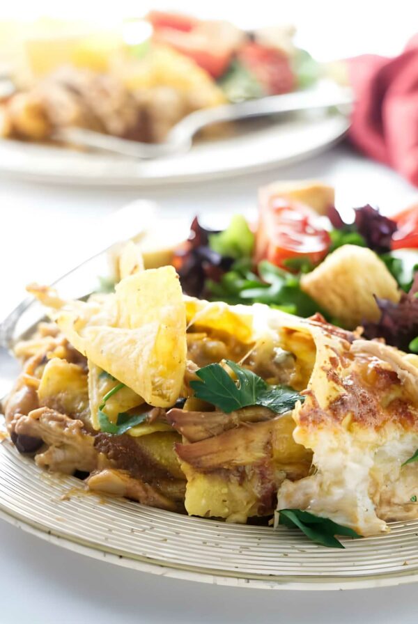 Cheesy tortilla chip bake with herbs beside vibrant salad.