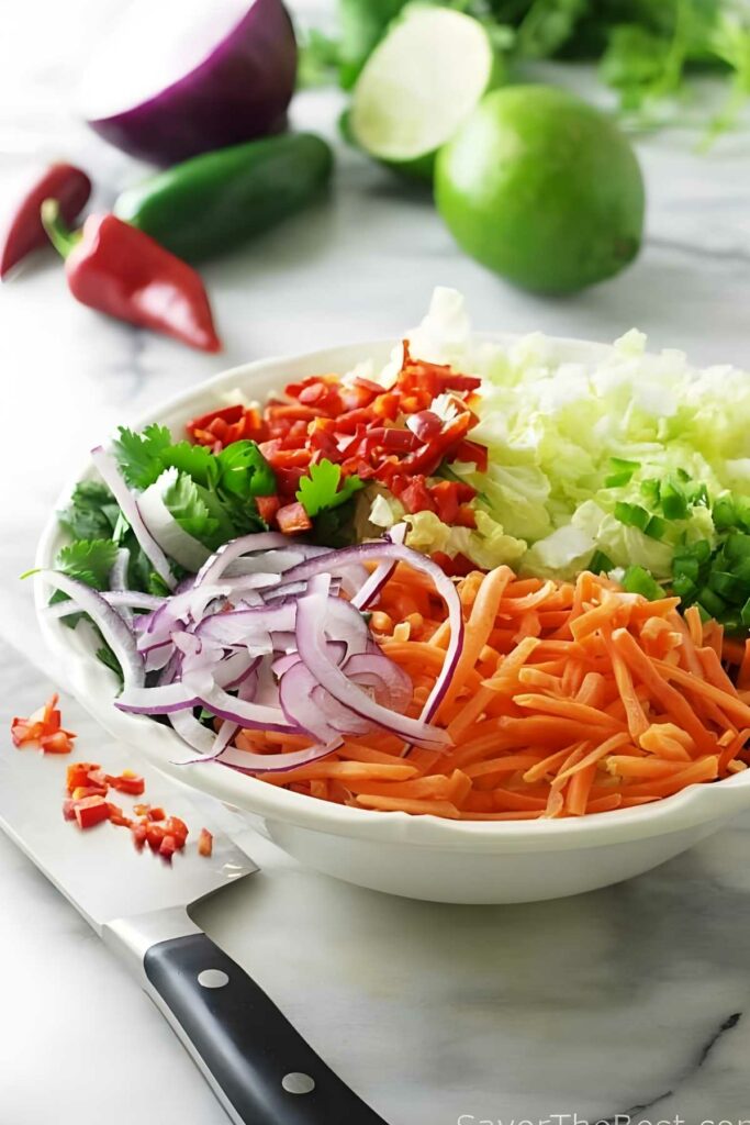 Bowl of fresh chopped vegetables with knife and produce in background.