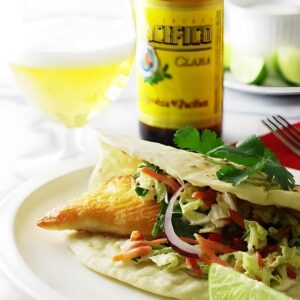 Fish taco with slaw and lime, beer and bottle in background.