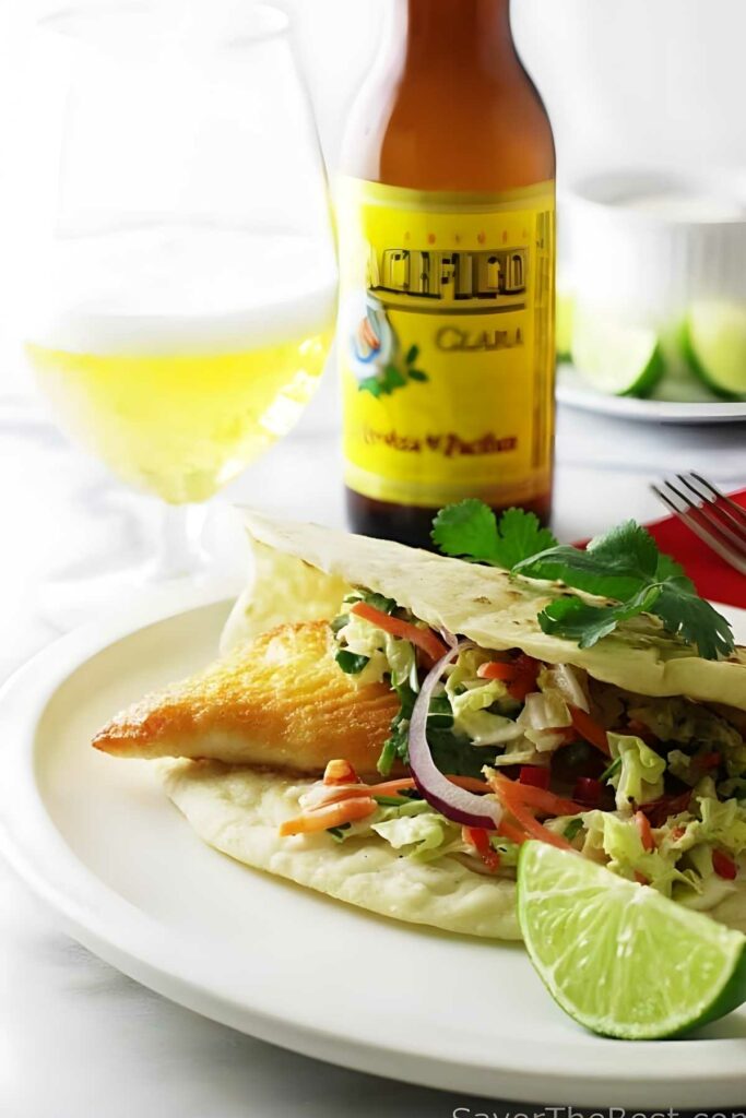 A tilapia fish taco with slaw and lime on a white plate.
