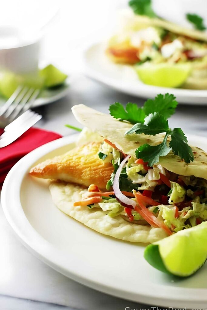 Tilapia fillet in a taco shell with spicy slaw; limes in the background.
