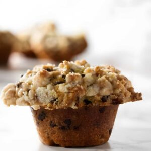 Close-up of chocolate chip muffin with streusel topping on marble surface.