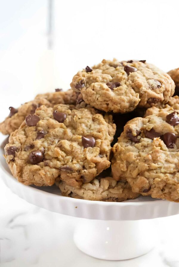 Stack of chocolate chip oatmeal cookies on white cake stand.
