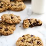 Oatmeal chocolate chip cookies with milk; one cookie broken showing gooey center.