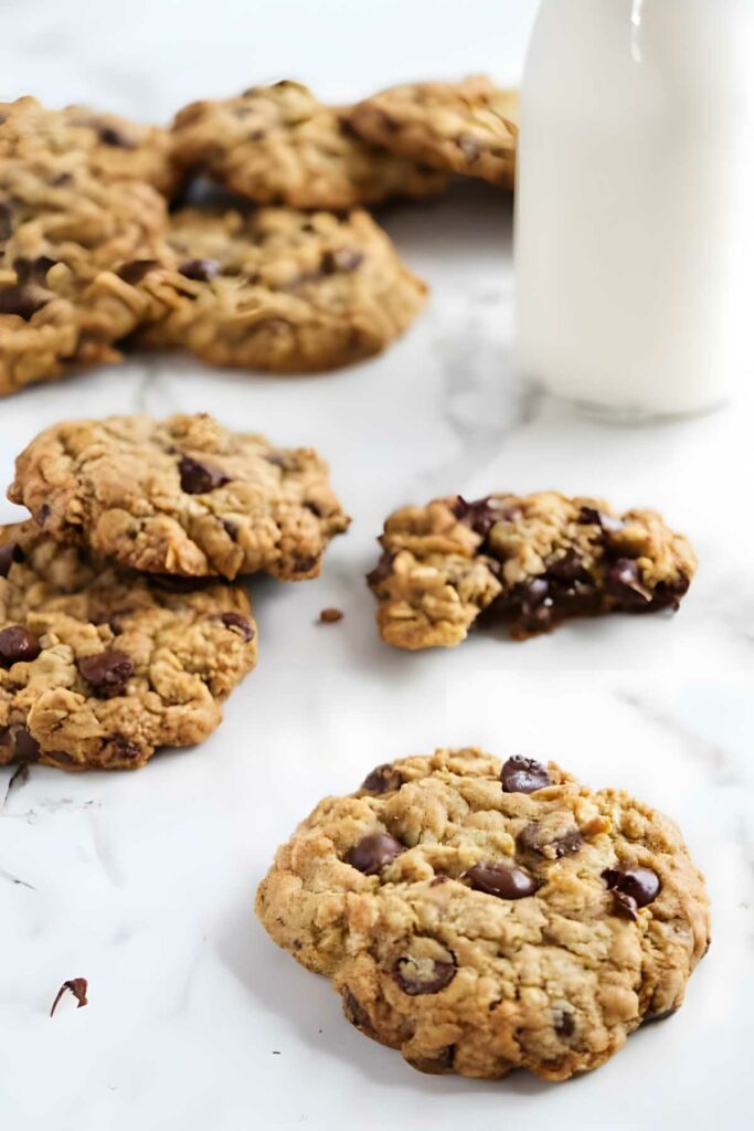Oatmeal chocolate chip cookies with milk; one cookie broken showing gooey center.