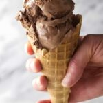Hand holding waffle cone with two scoops of stout beer chocolate ice cream.