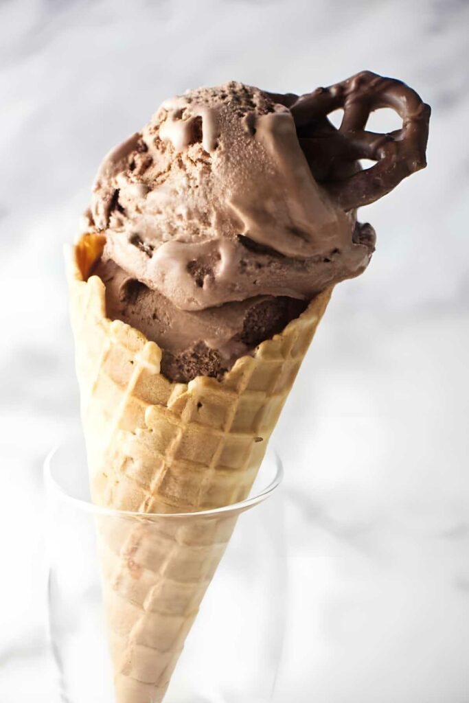 chocolate stout ice cream Waffle cone with chocolate and stout ice cream and pretzel, light blurred background.