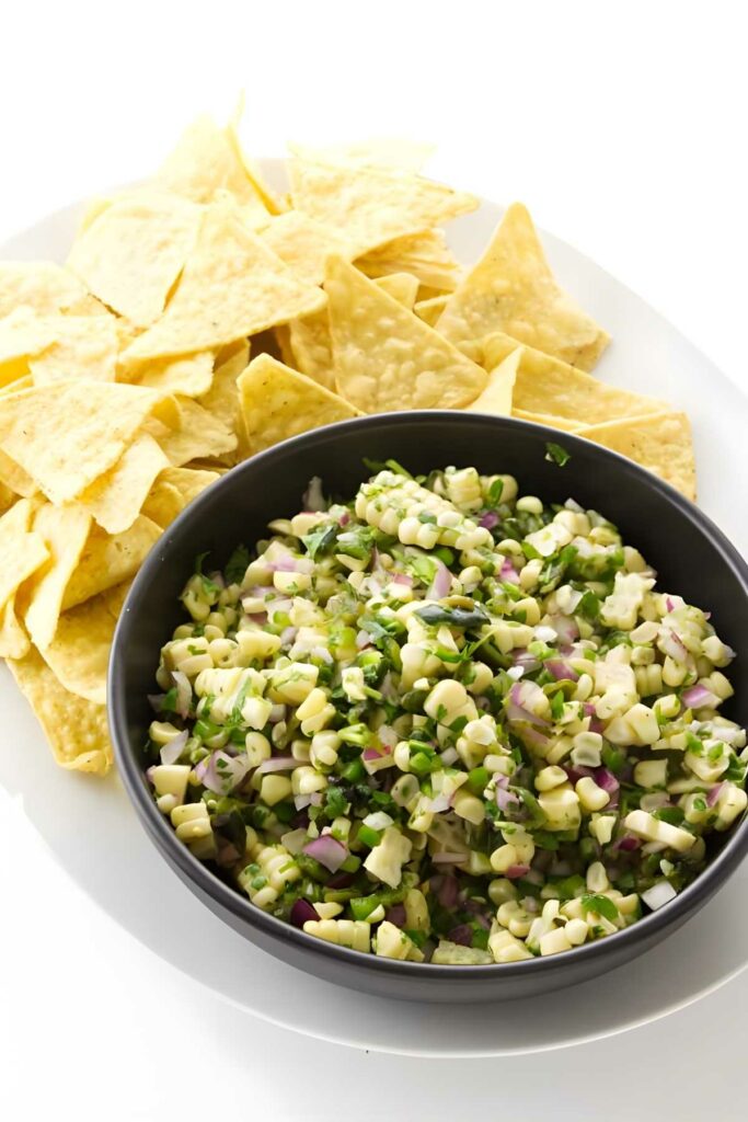 Black bowl of corn salsa with chips on a white plate.