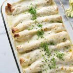 Baked crab meat enchiladas with melted cheese and herbs in a baking dish.