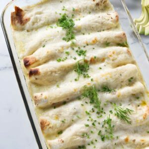 Baked crab meat enchiladas with melted cheese and herbs in a baking dish.