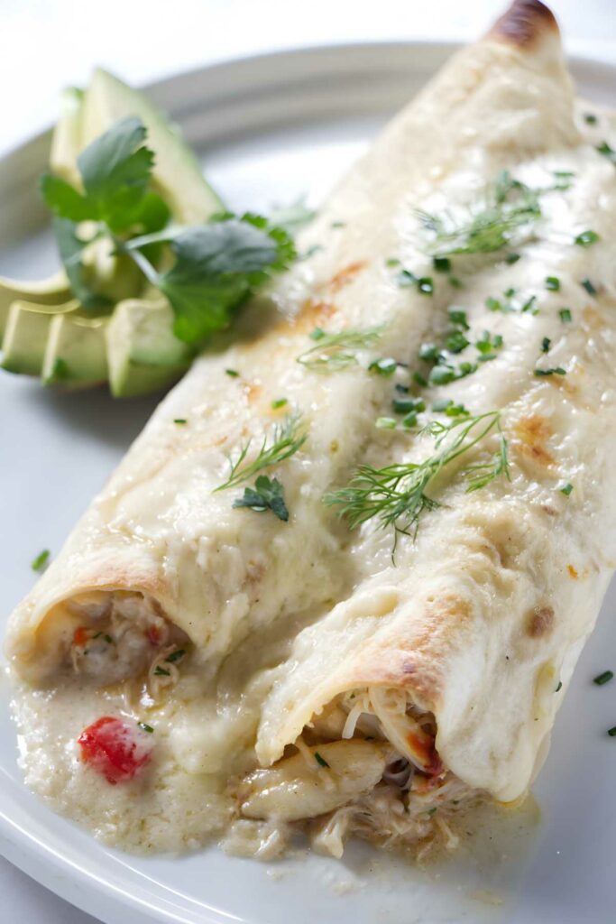 Lump crab meat enchiladas with white sauce, avocado slices, and fresh cilantro.
