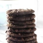 Stack of thin chocolate cookies on marble, blurred cookies behind.