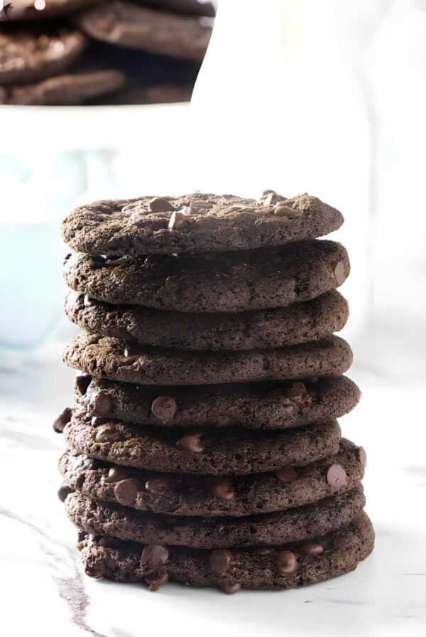 Stack of thin chocolate cookies on marble, blurred cookies behind.