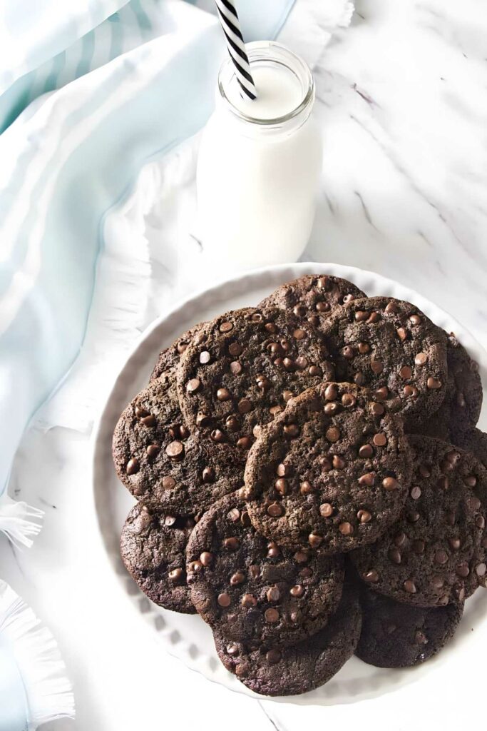 Plate of crispy thin chocolate cookies with milk and striped straw nearby.