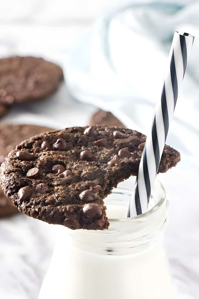 Bitten chocolate cookie on milk bottle with extra chocolate chips.
