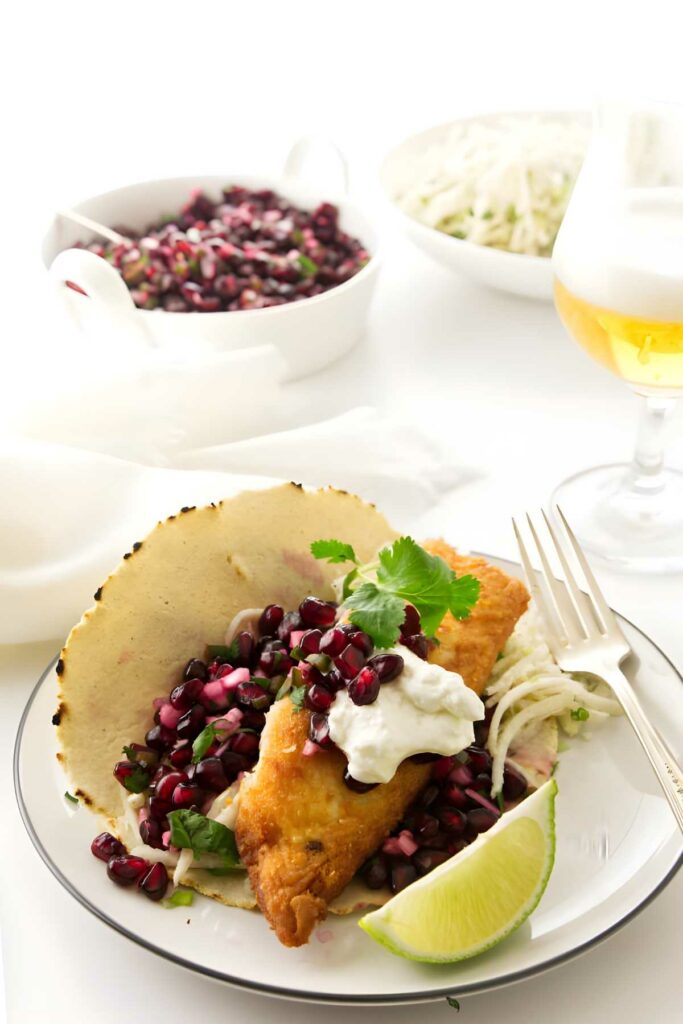 Fish taco with pomegranate salsa, sour cream, cilantro; beer and sides behind.