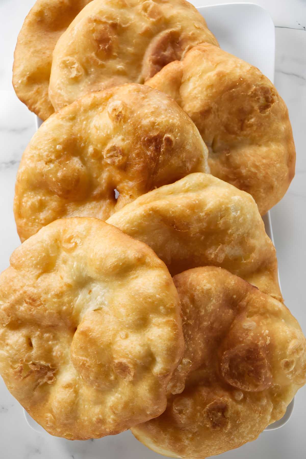 Plate of golden fry bread similar to fair bread stacked on white marble surface.