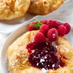 Fried dough with raspberry jam, sugar, fresh raspberries, and mint garnish.