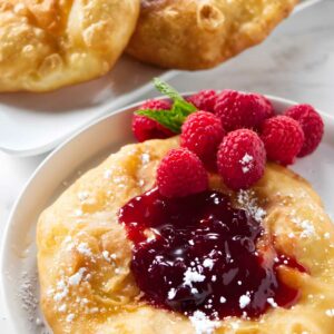 Fried dough with raspberry jam, sugar, fresh raspberries, and mint garnish.