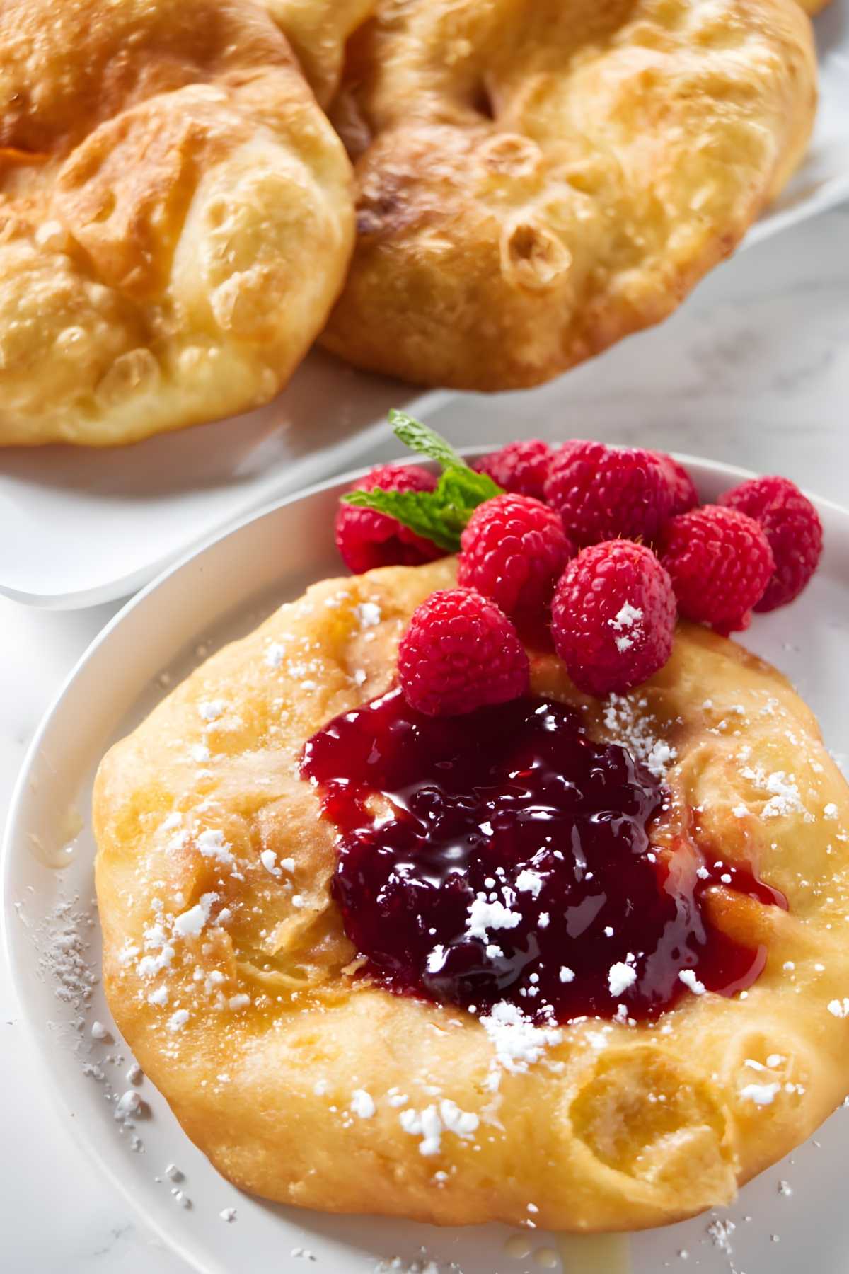 Carnival fry bread with raspberry jam, sugar, fresh raspberries, and mint garnish.