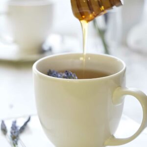 Honey drizzling into tea with lavender; second cup blurred in background.