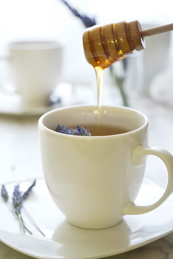 Honey drizzling into lavender tea with lavender bud next to it.